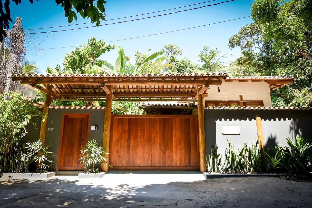 Fachada da Trancoso House com portão de madeira e pérgola
